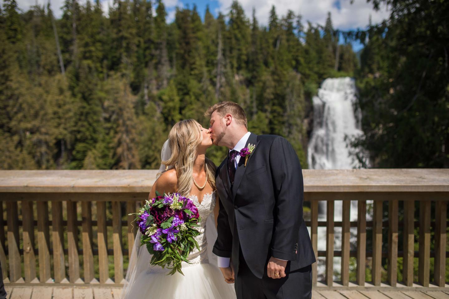 bride and groom kissing in front of waterfall