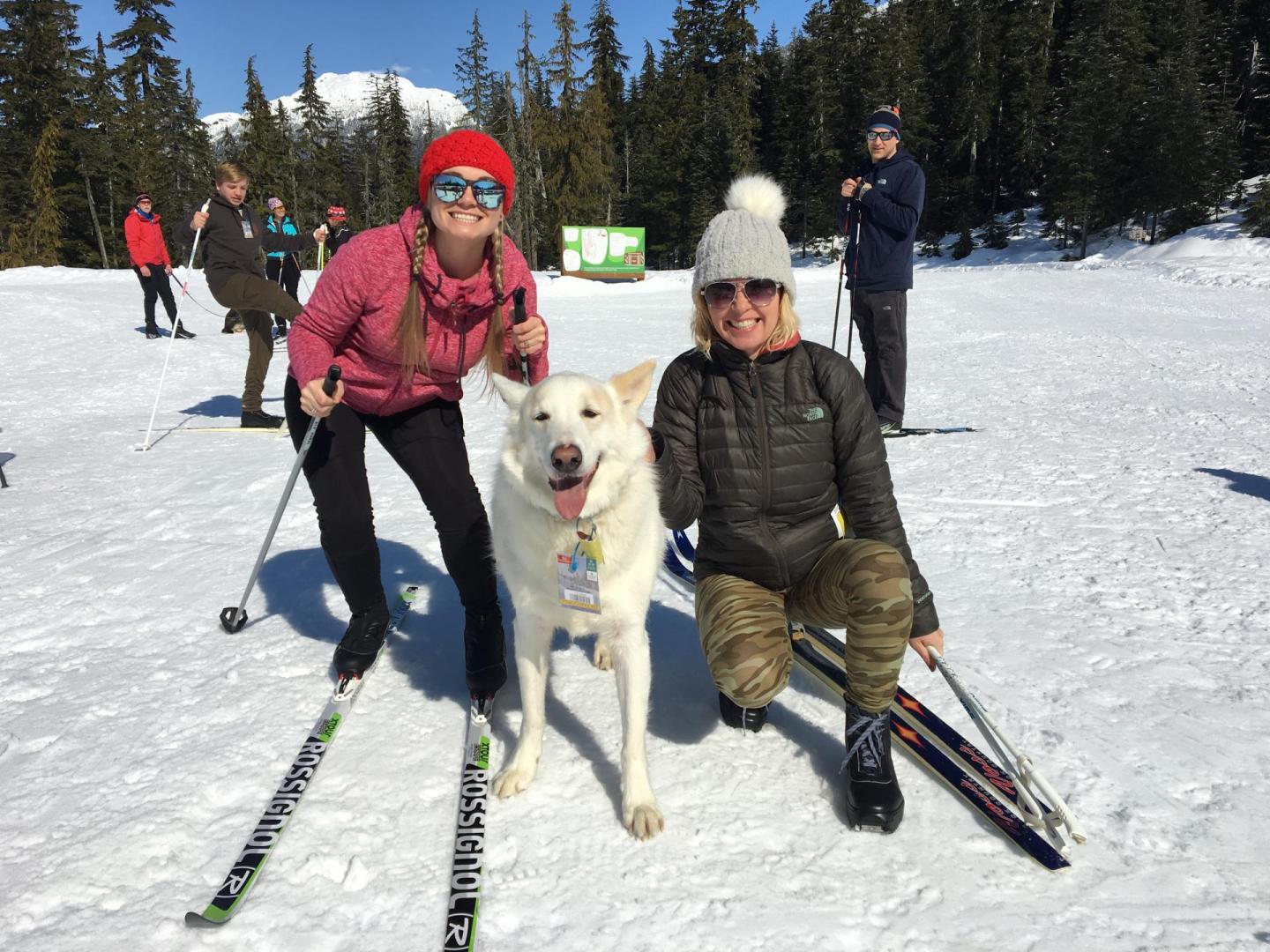 two women on skis smiling with white dog