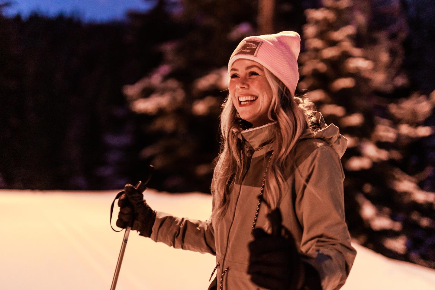 Woman smiling holding ski poles, outside in winter at night