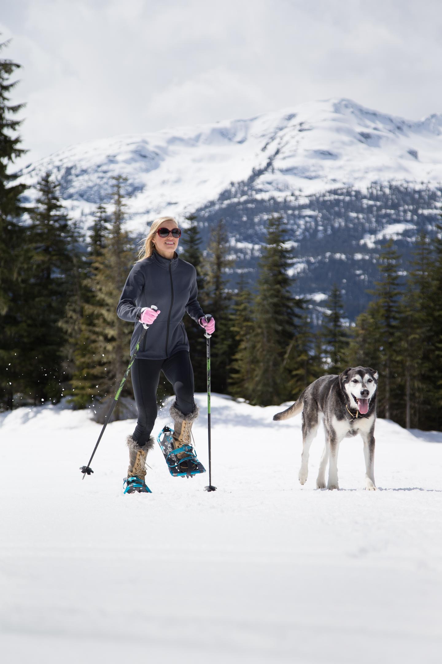 Woman snowshoeing with dog in mountains
