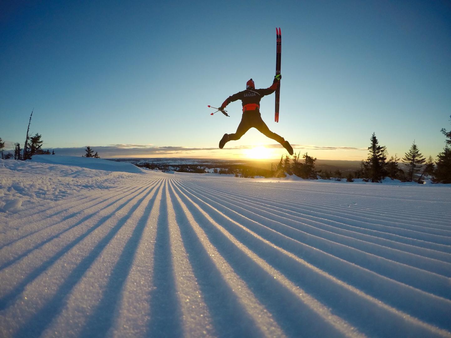 man jumping while holding skis, sun sets in the background
