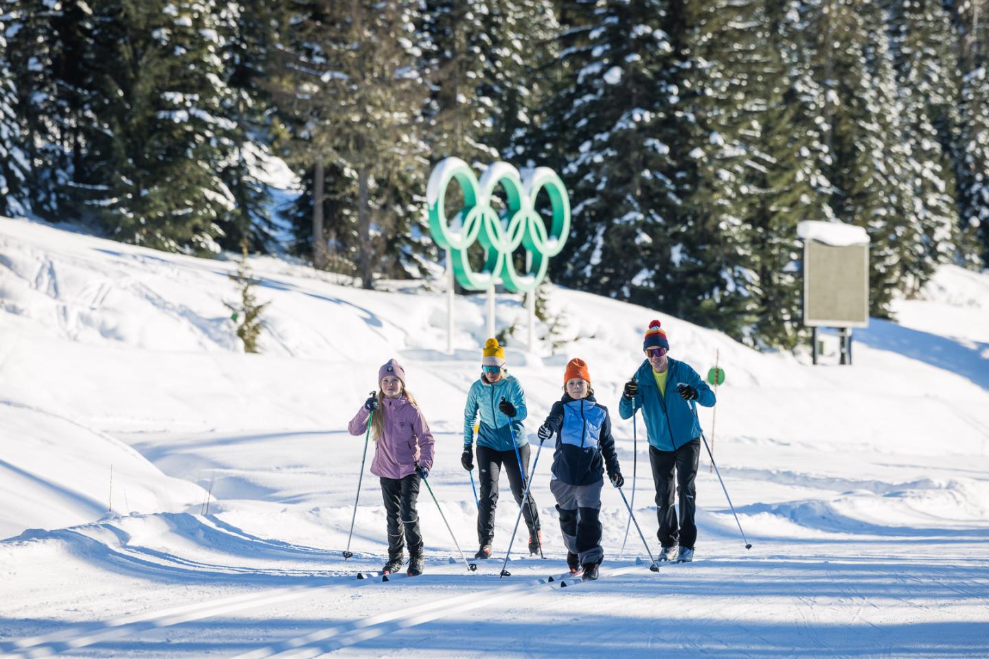 Four people cross-country skiing on a snowy trail with trees in the background.