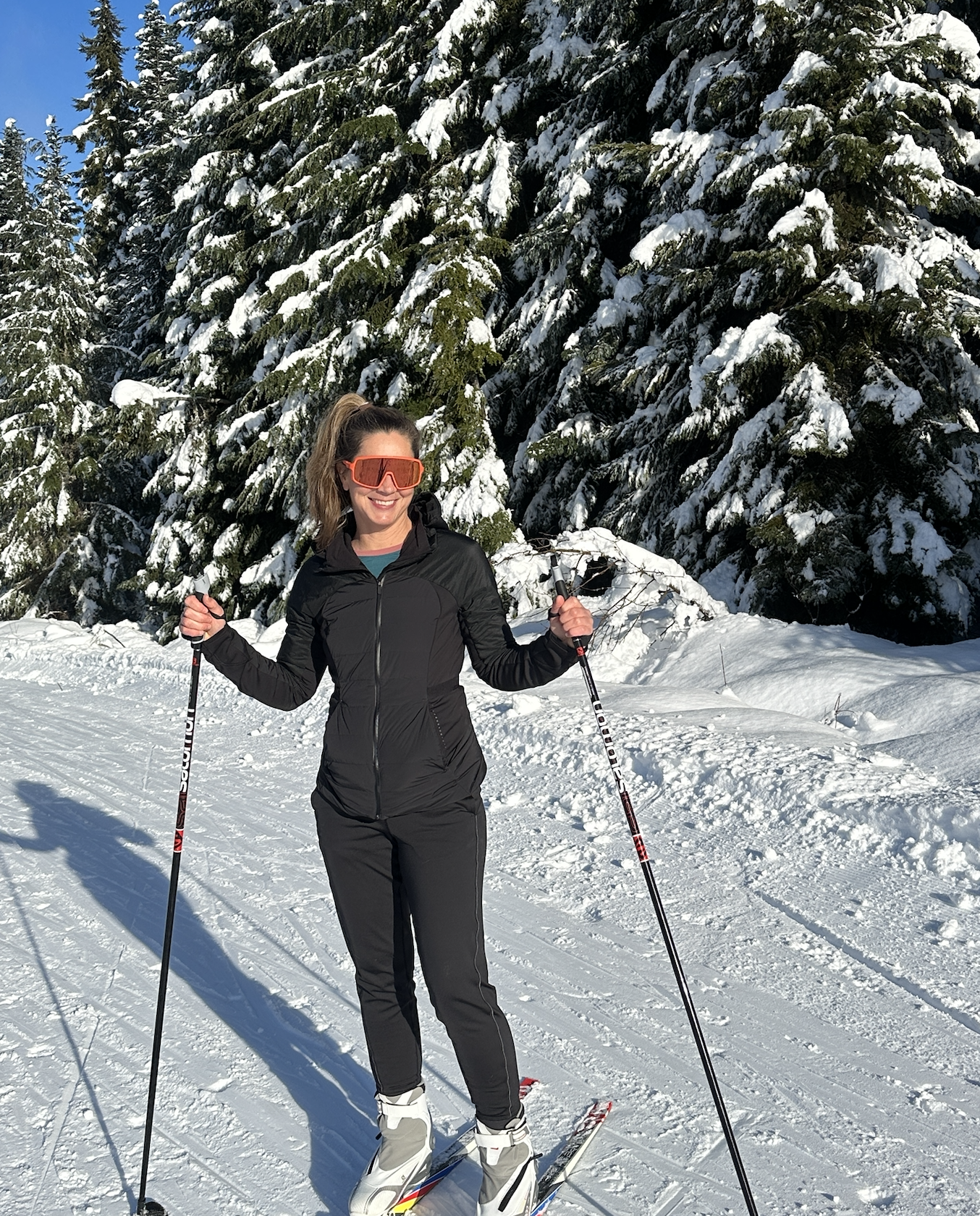Whistler Olympic Park Callaghan -Woman skiing on a sunny, snow-covered trail with tall, snowy trees.
