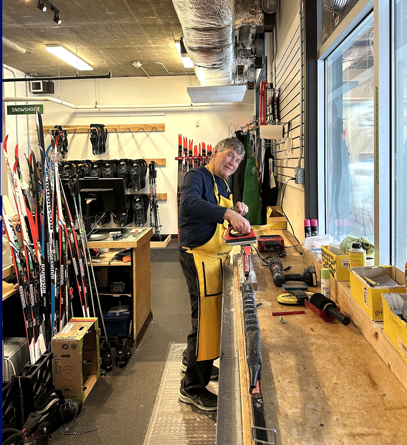Whistler Olympic Park Ski Tuning Man in workshop adjusting ski equipment, wearing a yellow apron.
