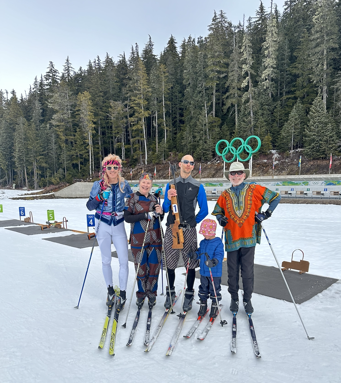 Whistler Olympic Park Group of people posing with skis on a snowy trail, surrounded by trees.