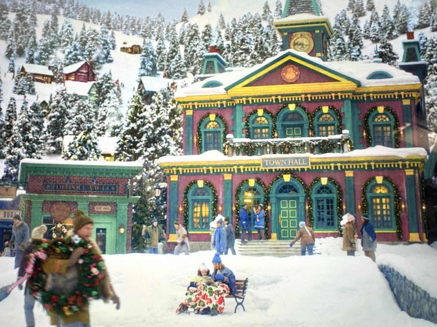 Snowy village scene with people outside a decorated building.