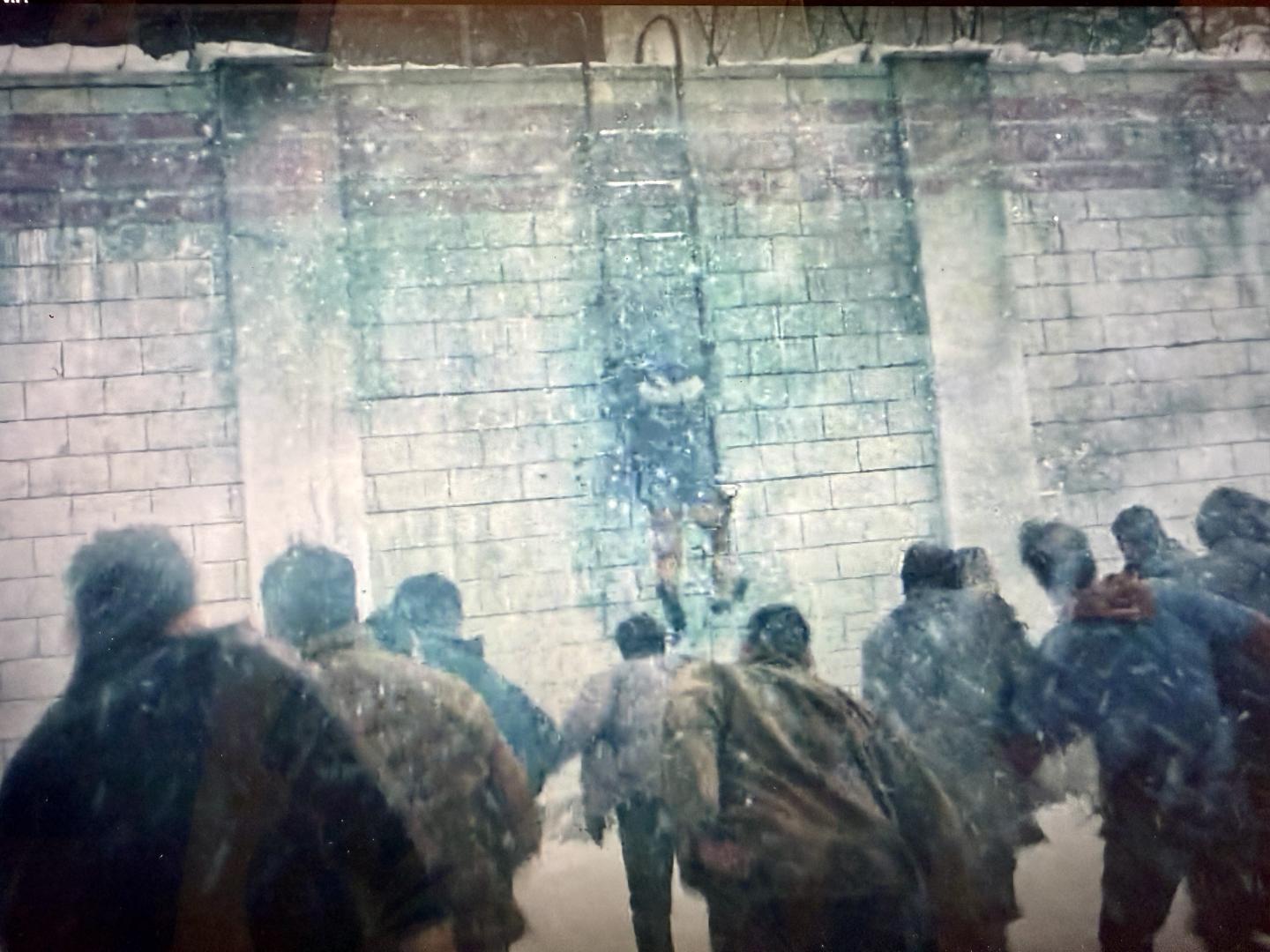 People running in a snowstorm towards a tall brick wall.