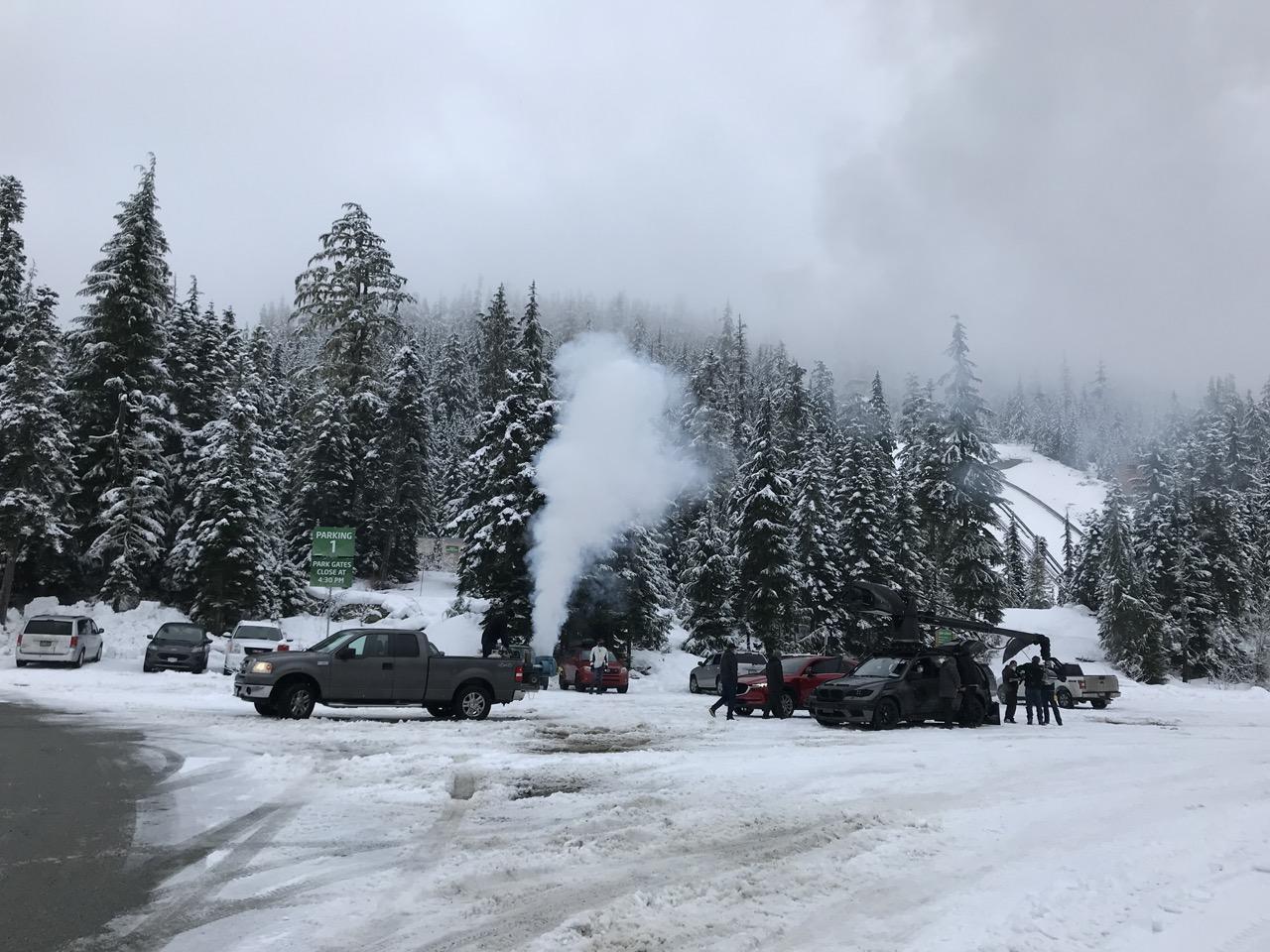 Snowy forest with parked cars and people around a campfire.