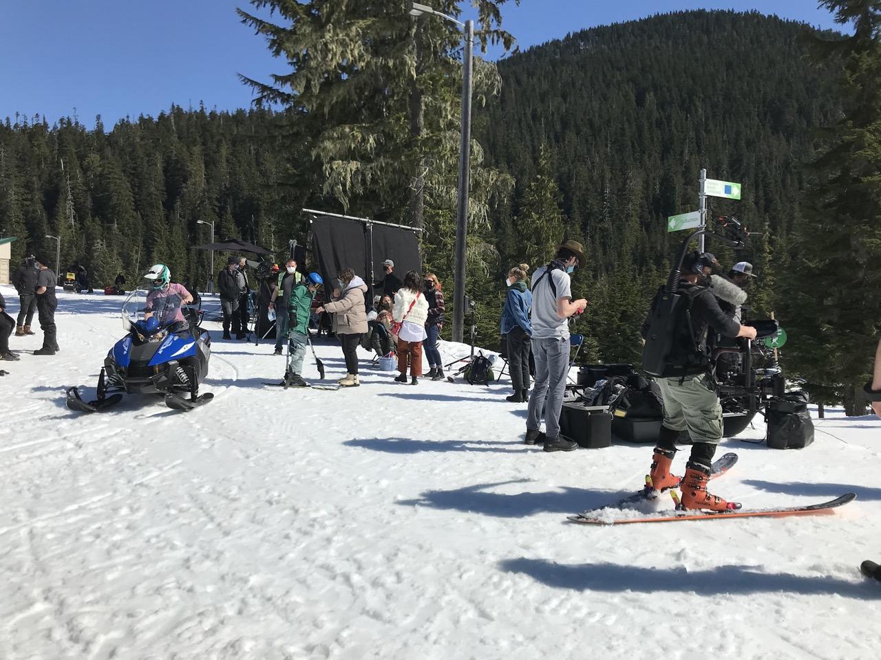 Snowy mountain scene with people skiing and snowboarding, trees in the background.