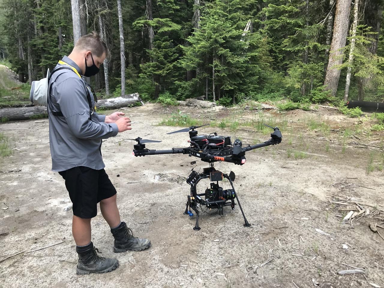 Man standing in forest next to a large drone.