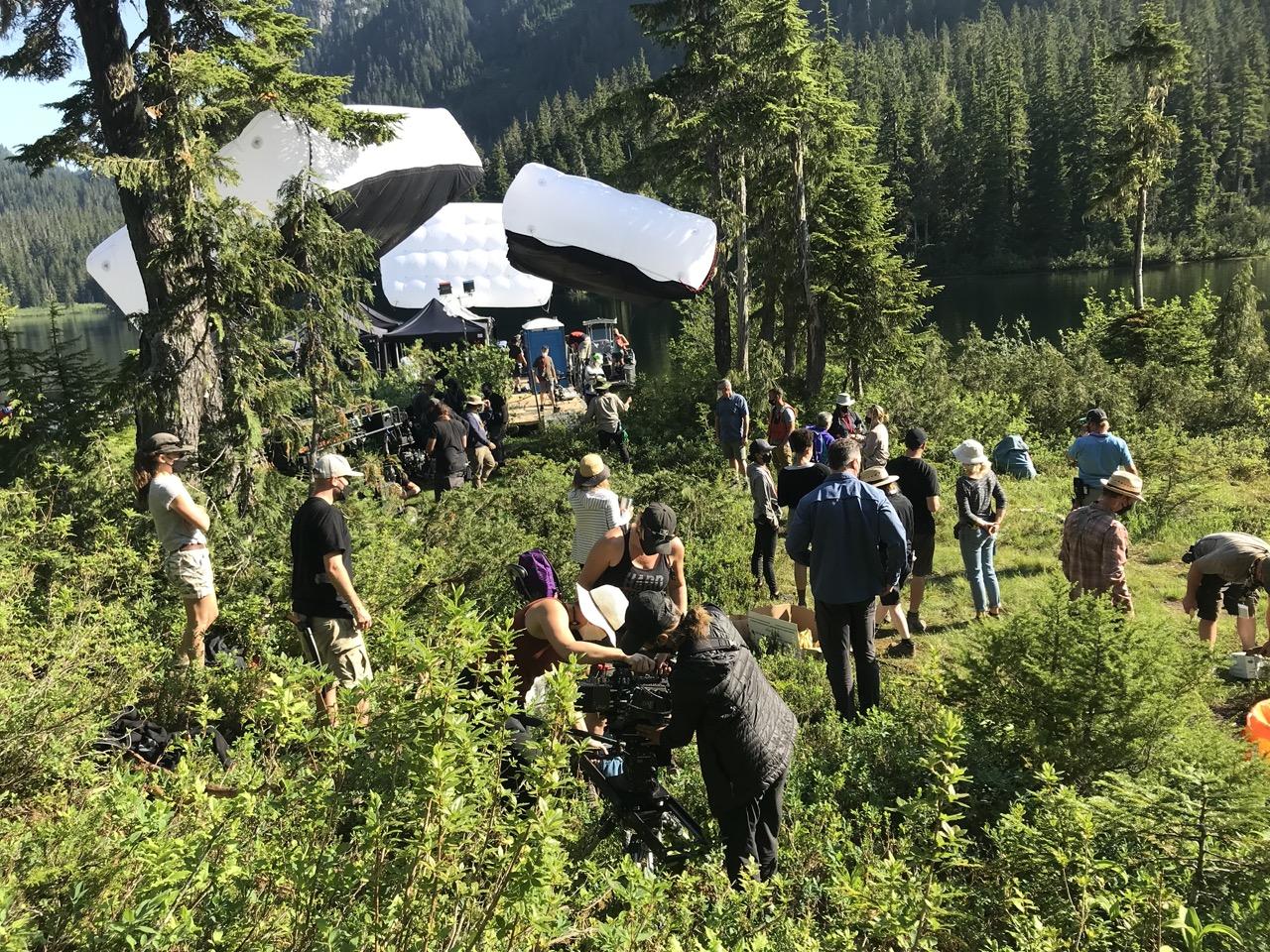 Film crew working in a forested area with tall trees and equipment.