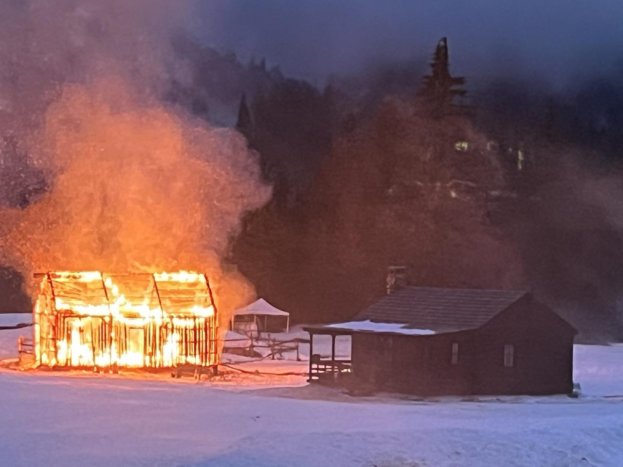 Burning house next to a snowy cabin at dusk.