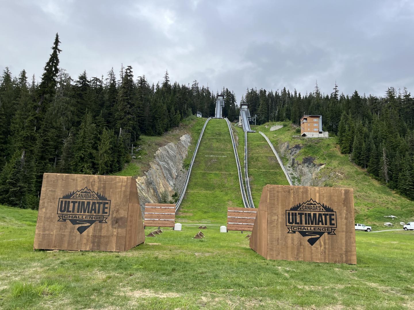 Ski jump ramp on a grassy hill with two wooden obstacle signs.