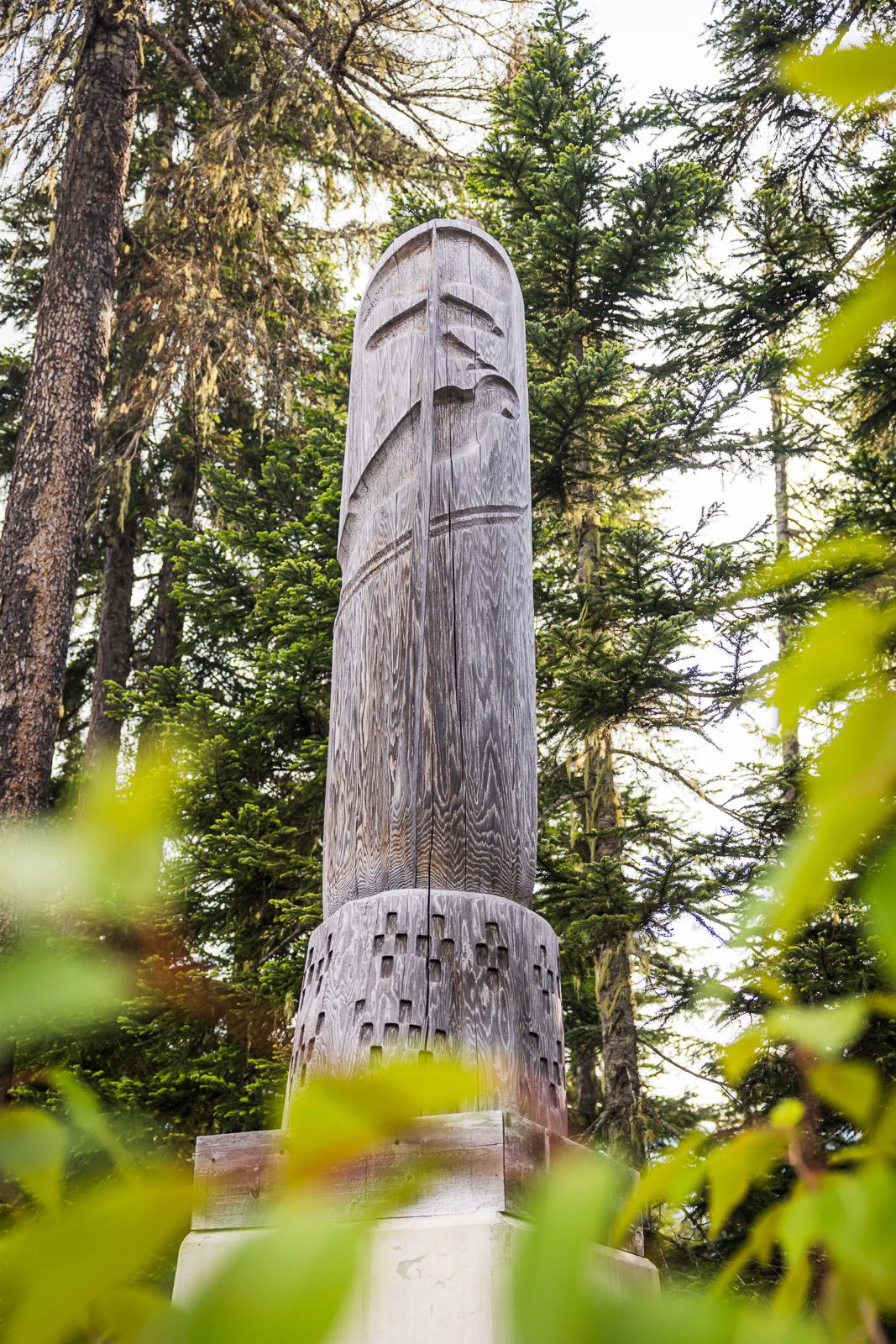 Tall wooden totem pole surrounded by lush green trees.