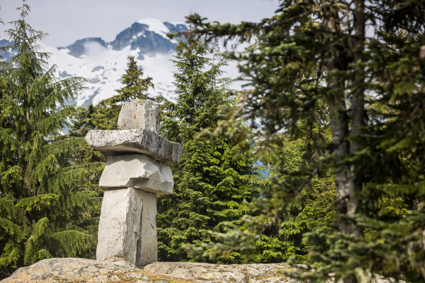 Stone sculpture amid green trees with mountains in the background.