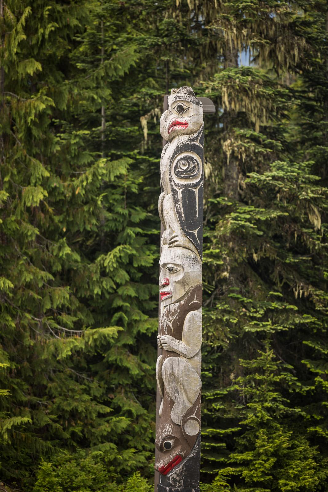 Tall totem pole with animal carvings set against lush green forest.