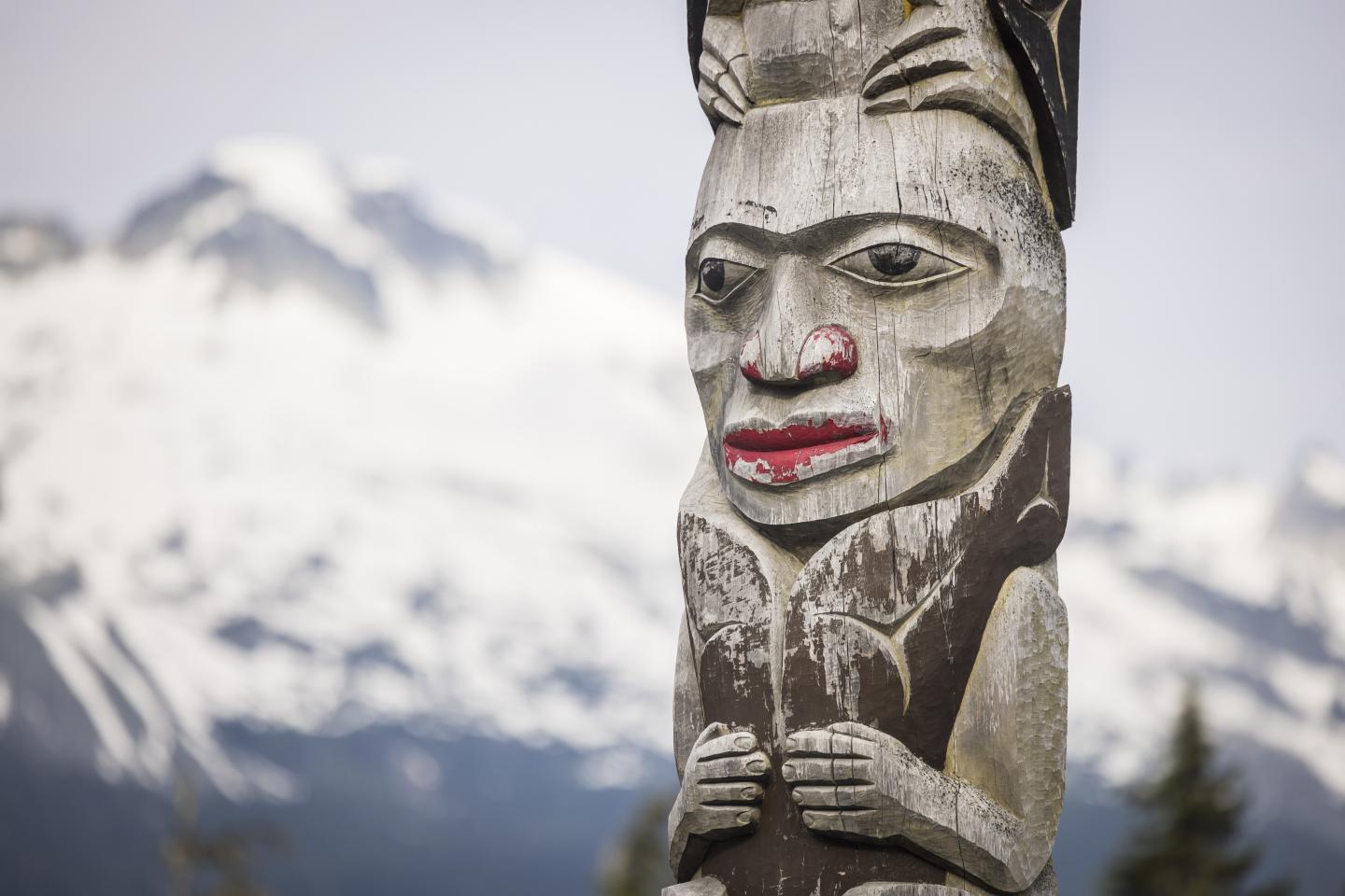 Carved totem pole with snowy mountains in the background.