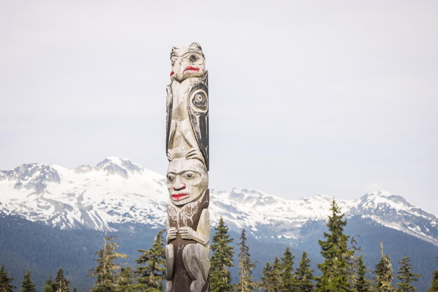 Totem pole with mountains and trees in the background.