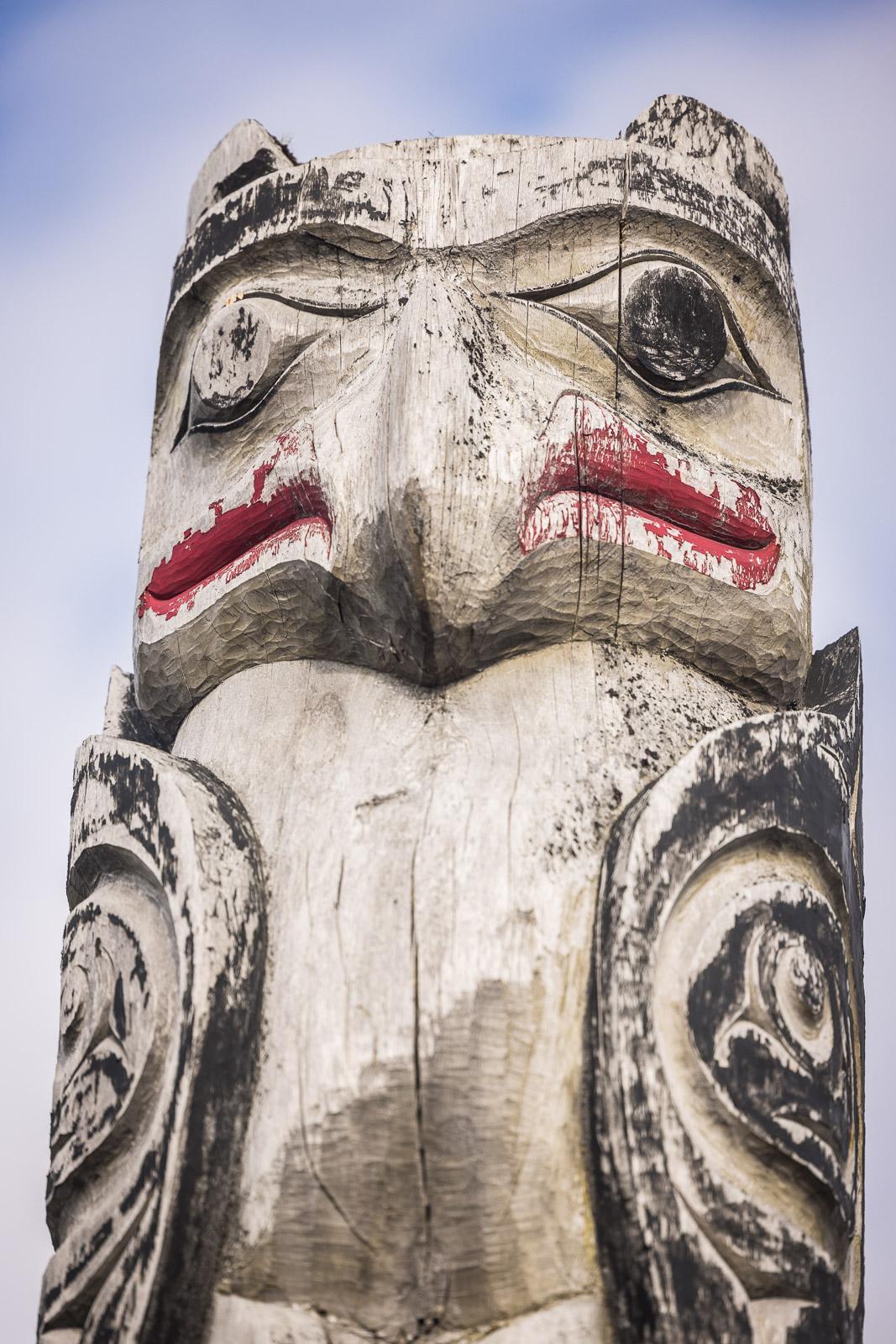 Totem pole with carved face and red accents against a blue sky.