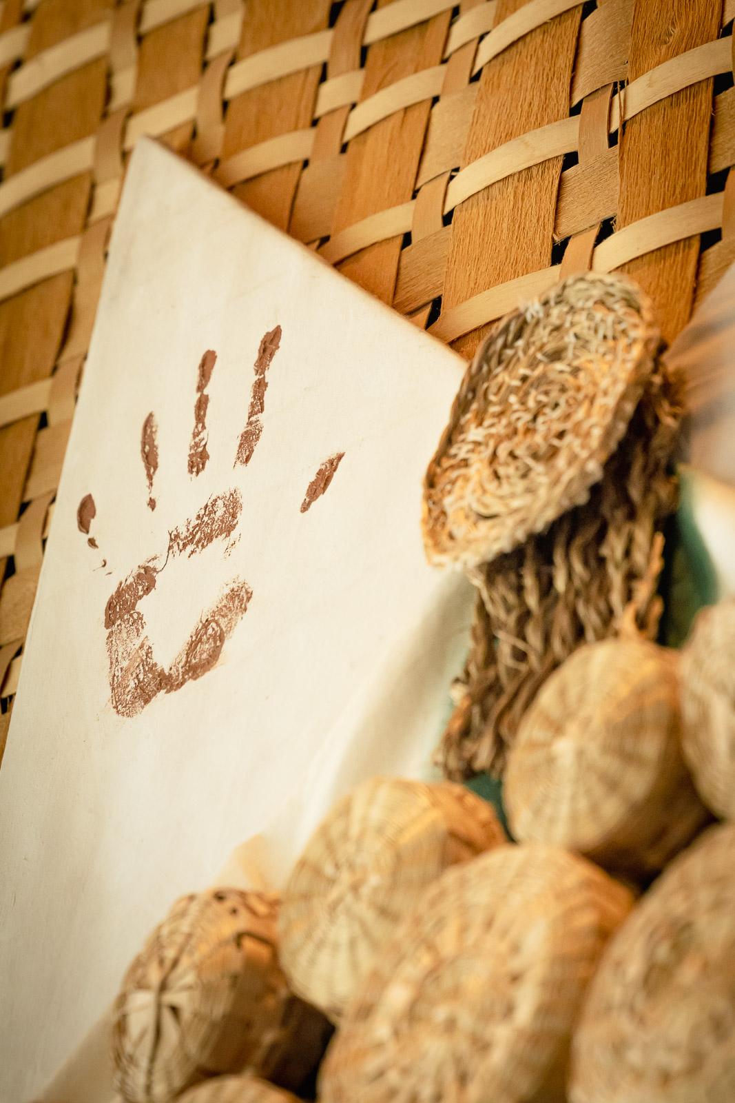 Handprint on paper with woven background and natural fiber balls.