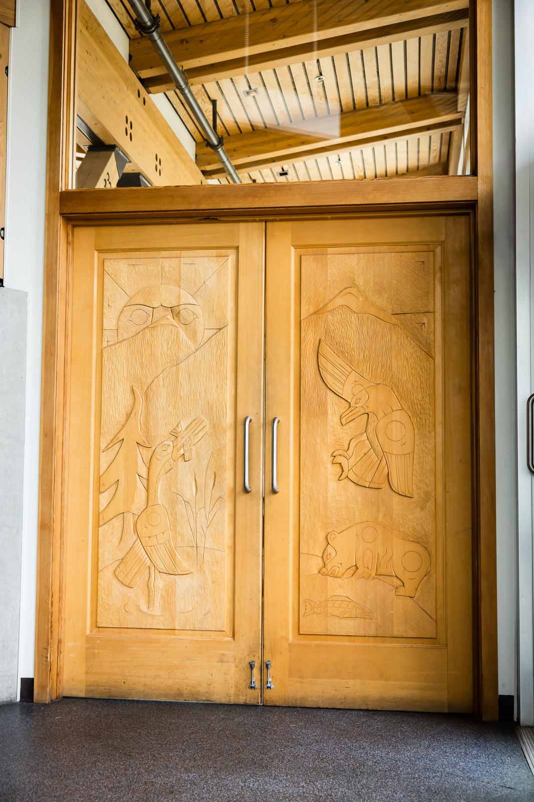 Wooden double doors with carved designs under a high ceiling.