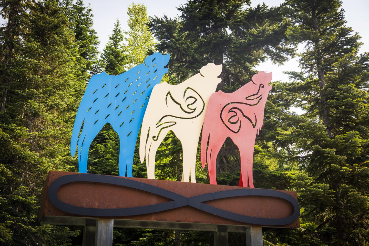 Three colorful bear sculptures on a signpost in a forest setting.
