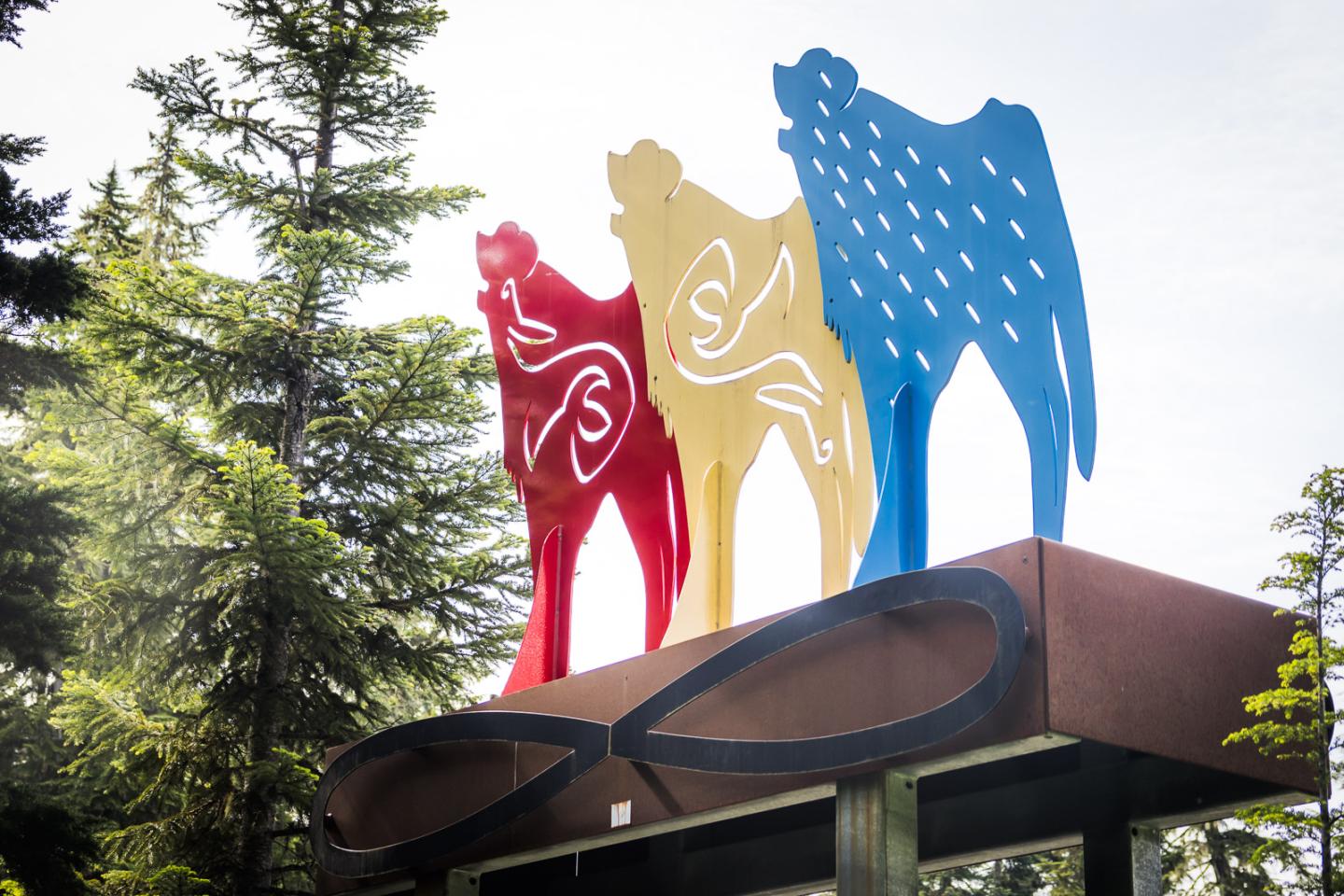 Three colorful figures atop a building, surrounded by trees.