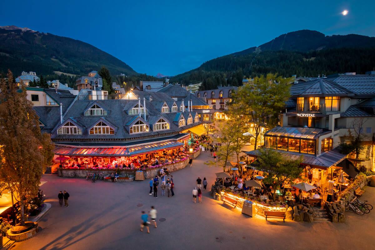 Village square at dusk with lit buildings and mountains in the background.