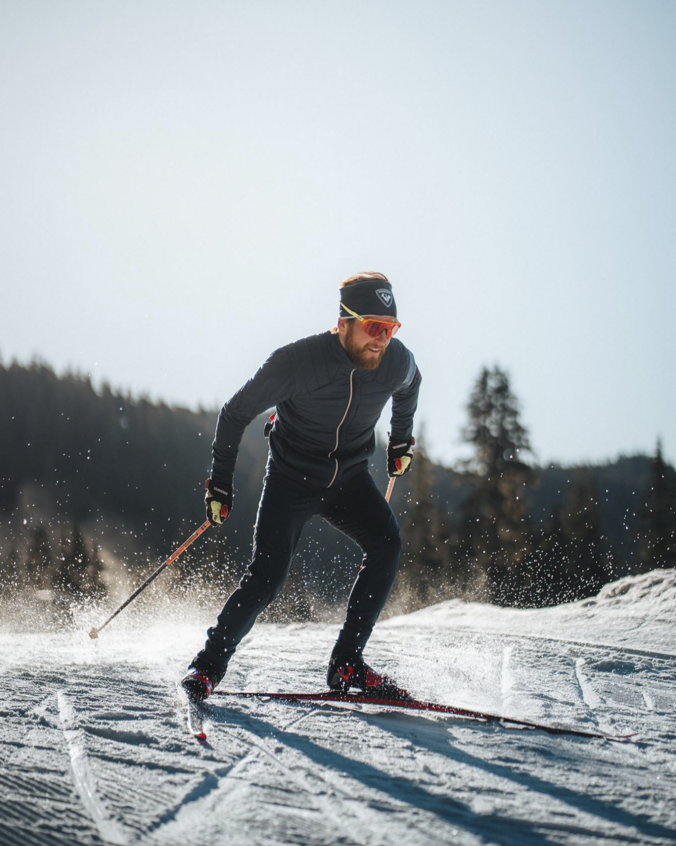 Cross-country skier in motion on a snowy trail under a clear sky.