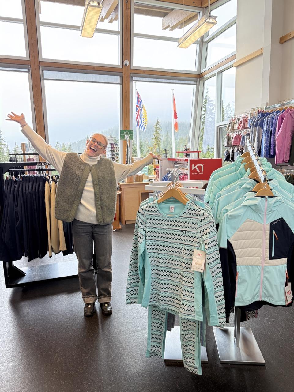 Store interior with clothes on racks, person smiling with arms outstretched.