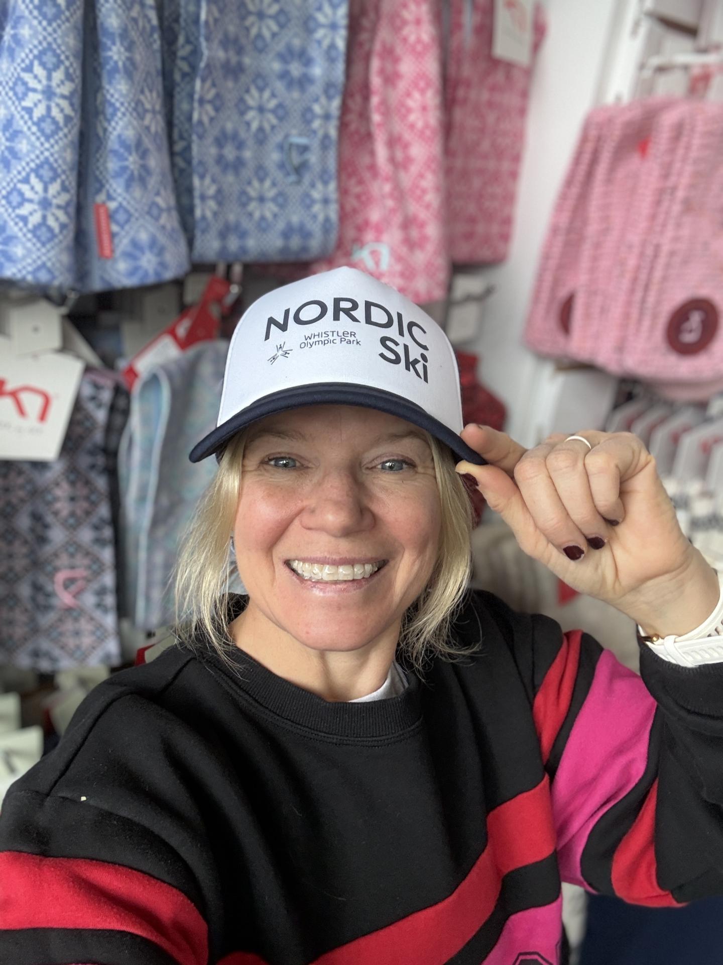 Woman smiling, wearing a "Nordic Ski" cap, surrounded by patterned textiles.