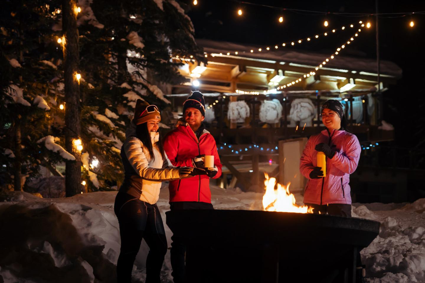 Group enjoying a firepit in a snowy, festive setting at night.