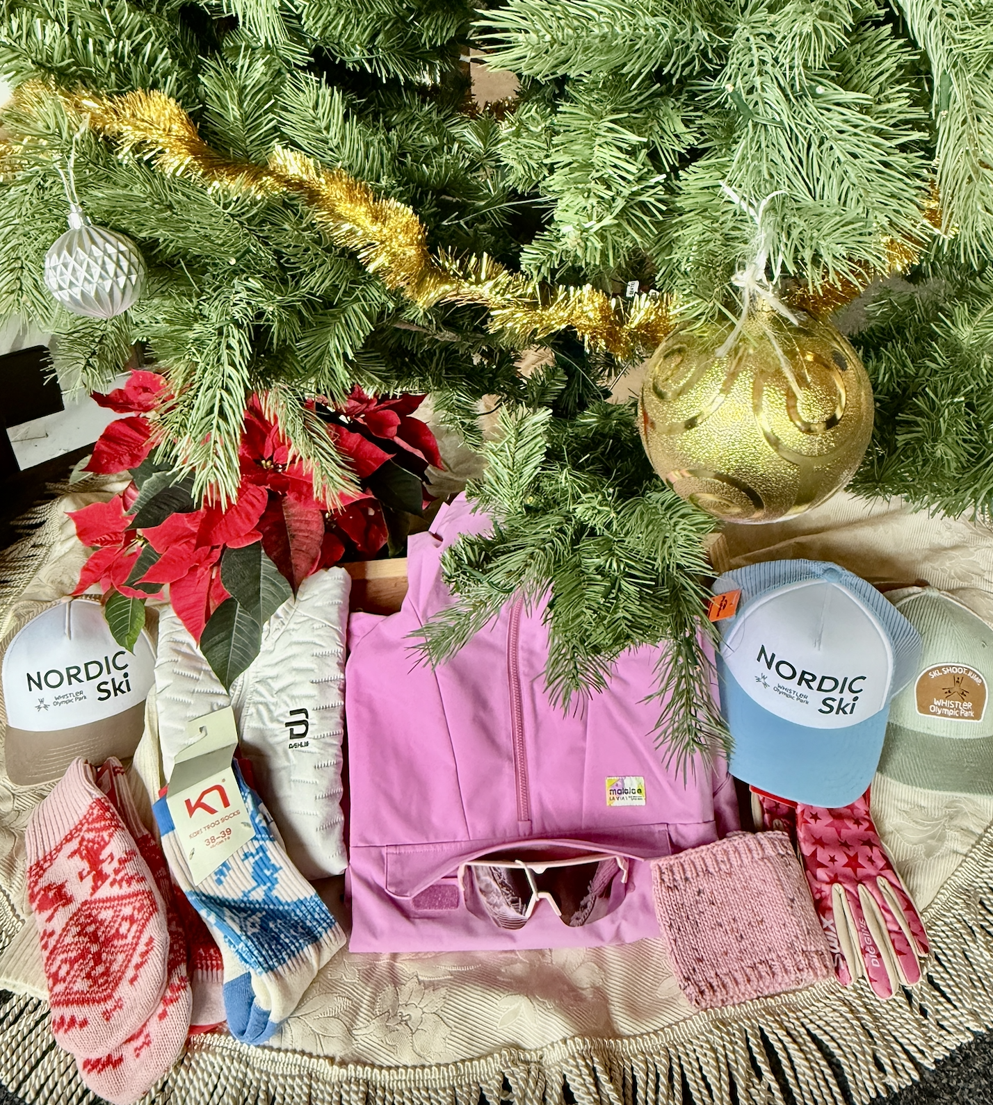 Gifts under a Christmas tree include clothing, hats, and red mittens.