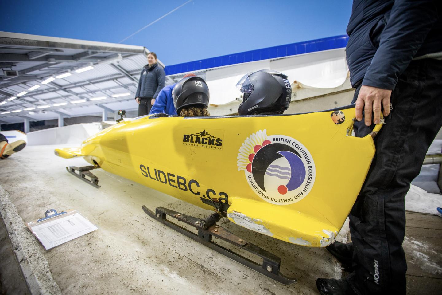 Yellow bobsled with two helmeted riders, preparing on an icy track.
