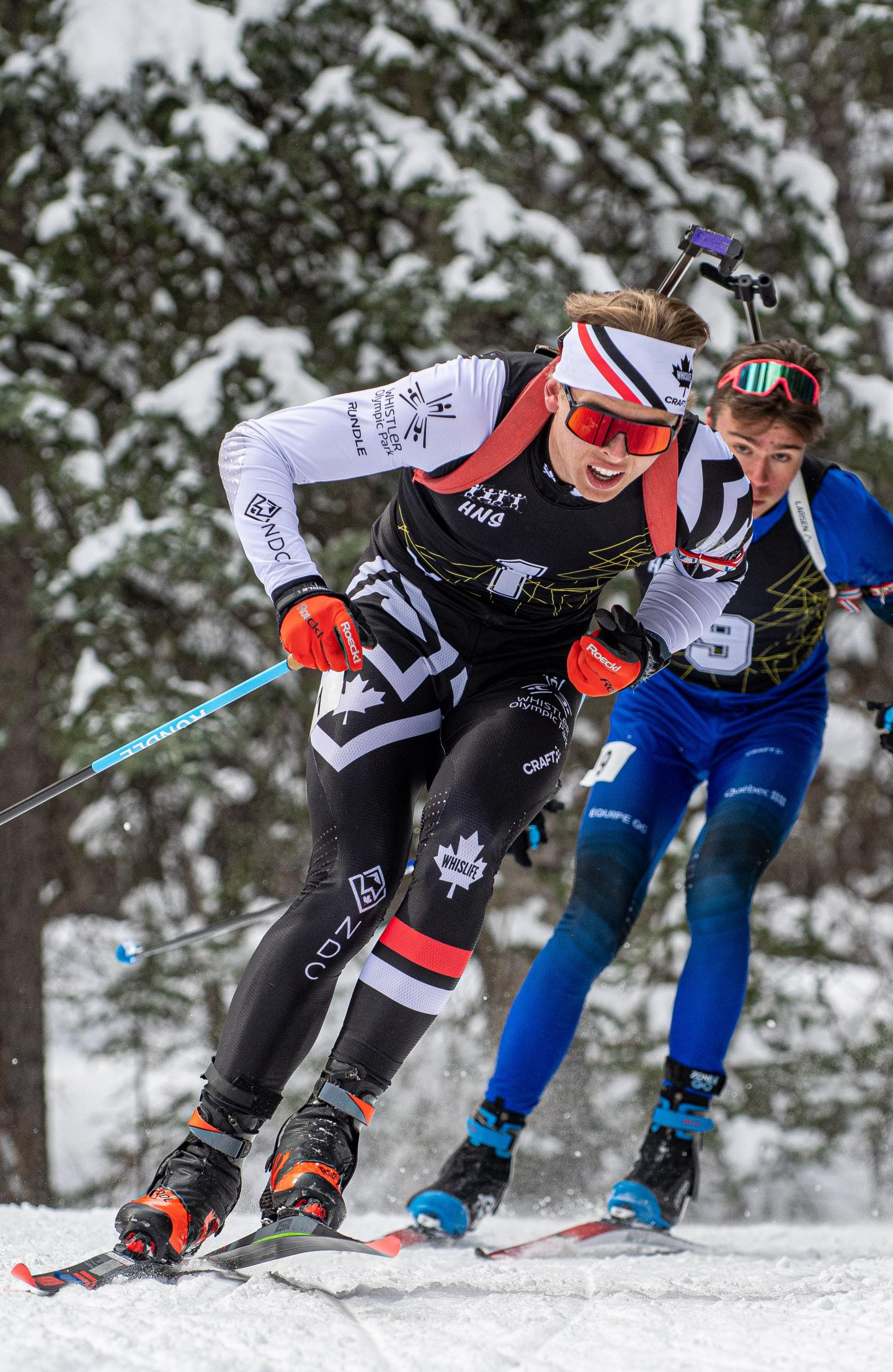 Two skiers racing in a snow-covered forest, wearing colorful gear and focused expressions.