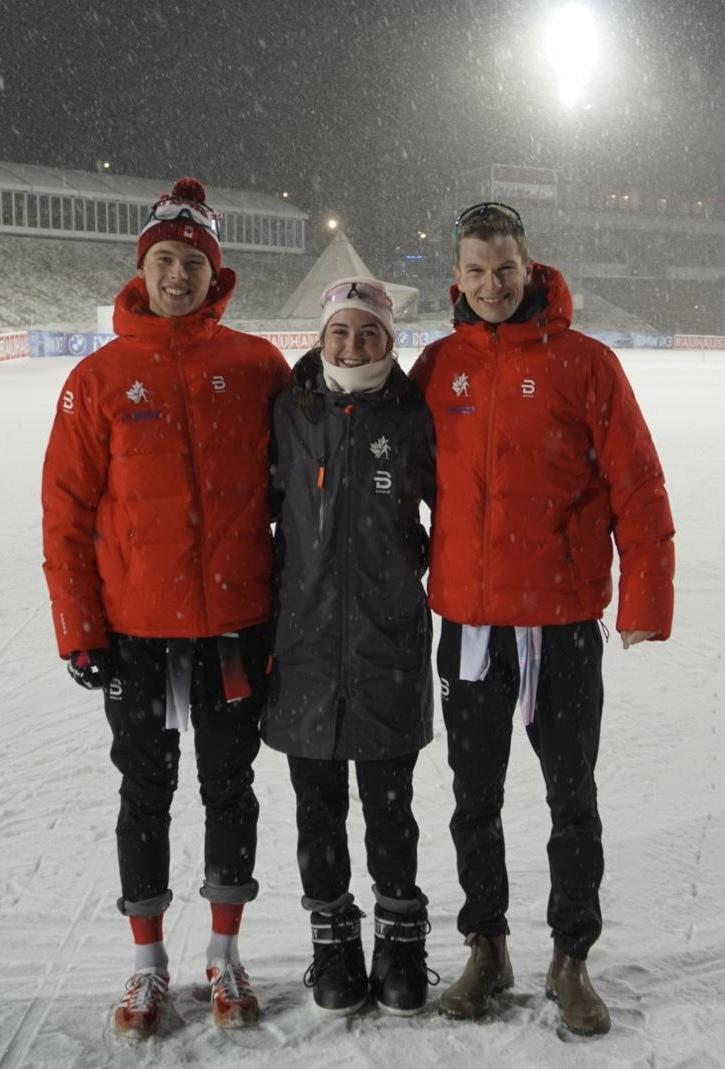 Three people in red jackets standing on a snowy field at night.