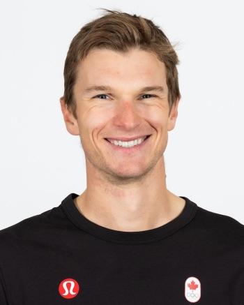 Smiling man in a black shirt with red logos on a white background.
