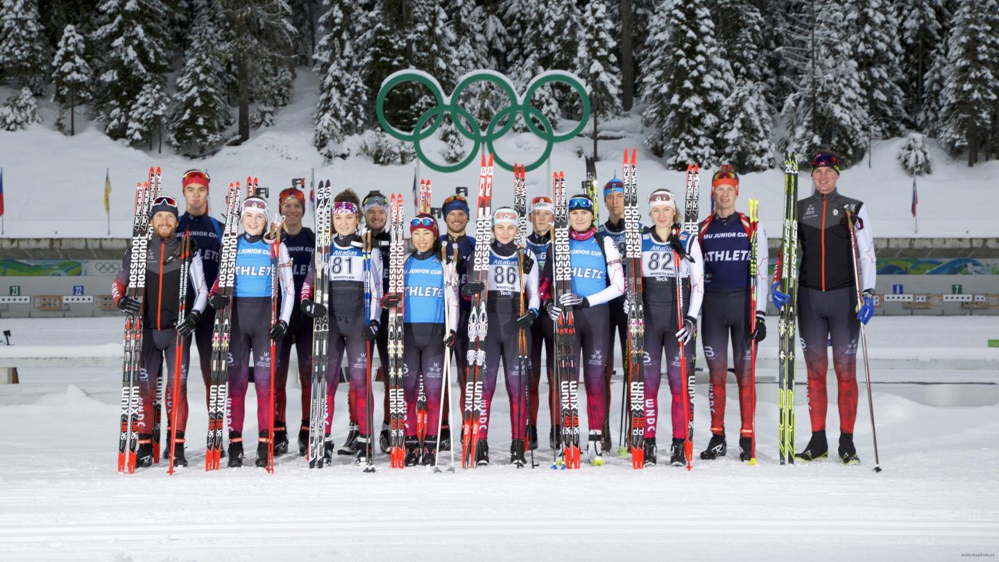 Cross-country skiers pose together in snowy landscape under Olympic rings.