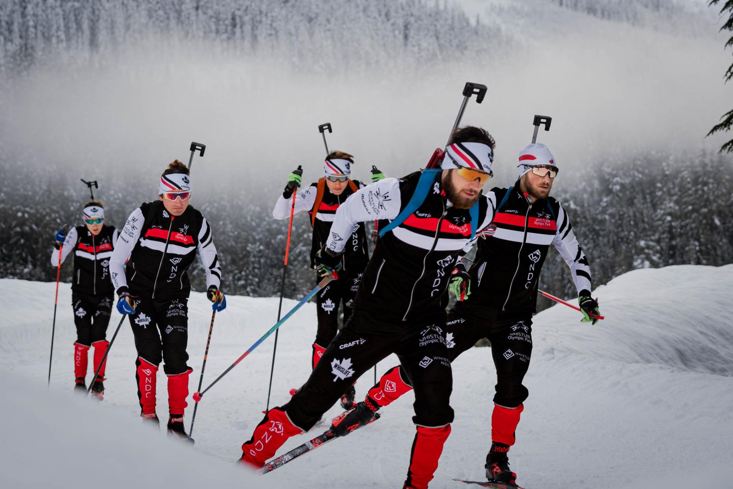Skiers in black outfits and red boots traversing snowy landscape.