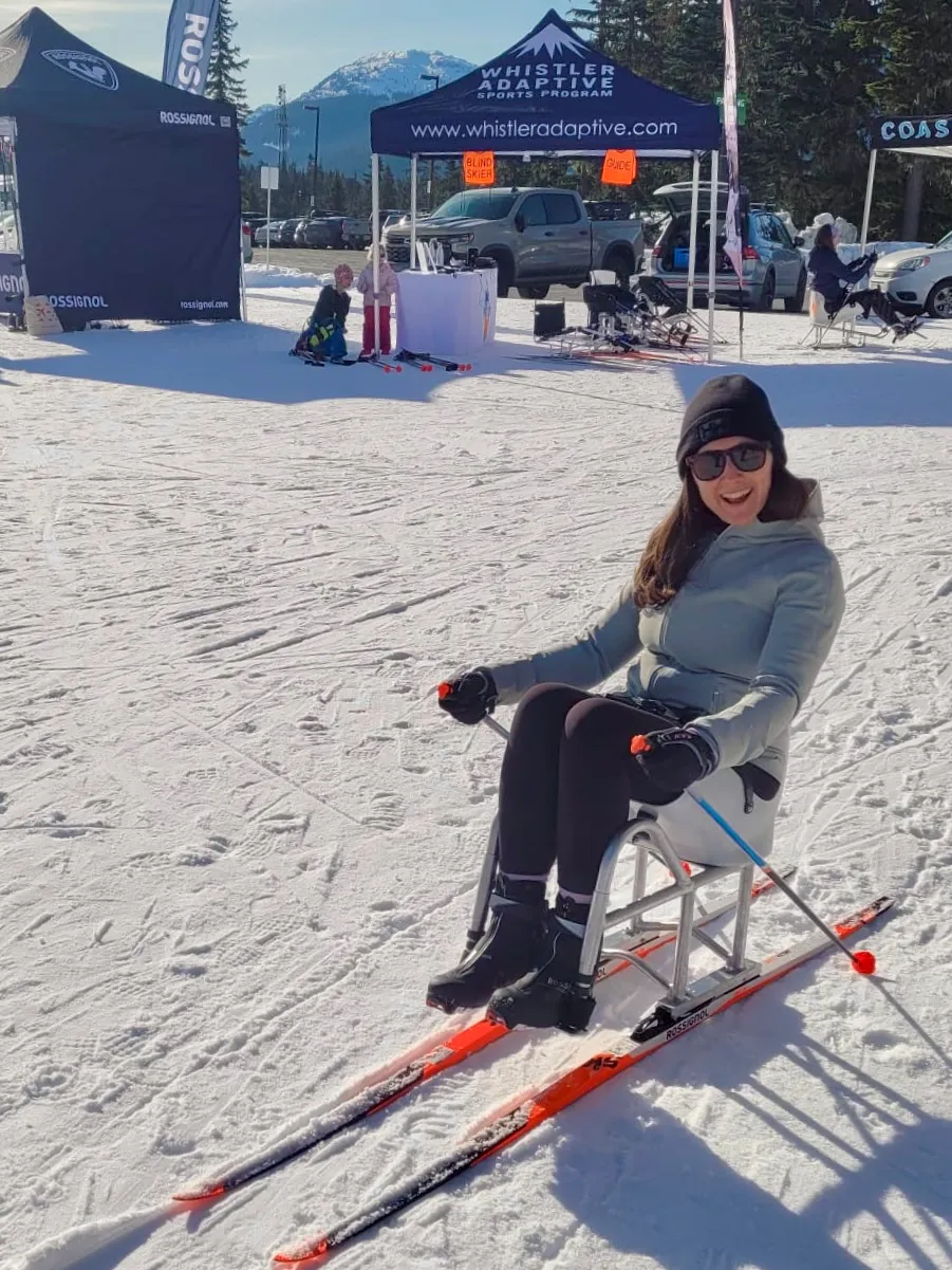 Sophia Krstin Person in a sit-ski on a snowy mountain, smiling, with event tents nearby.