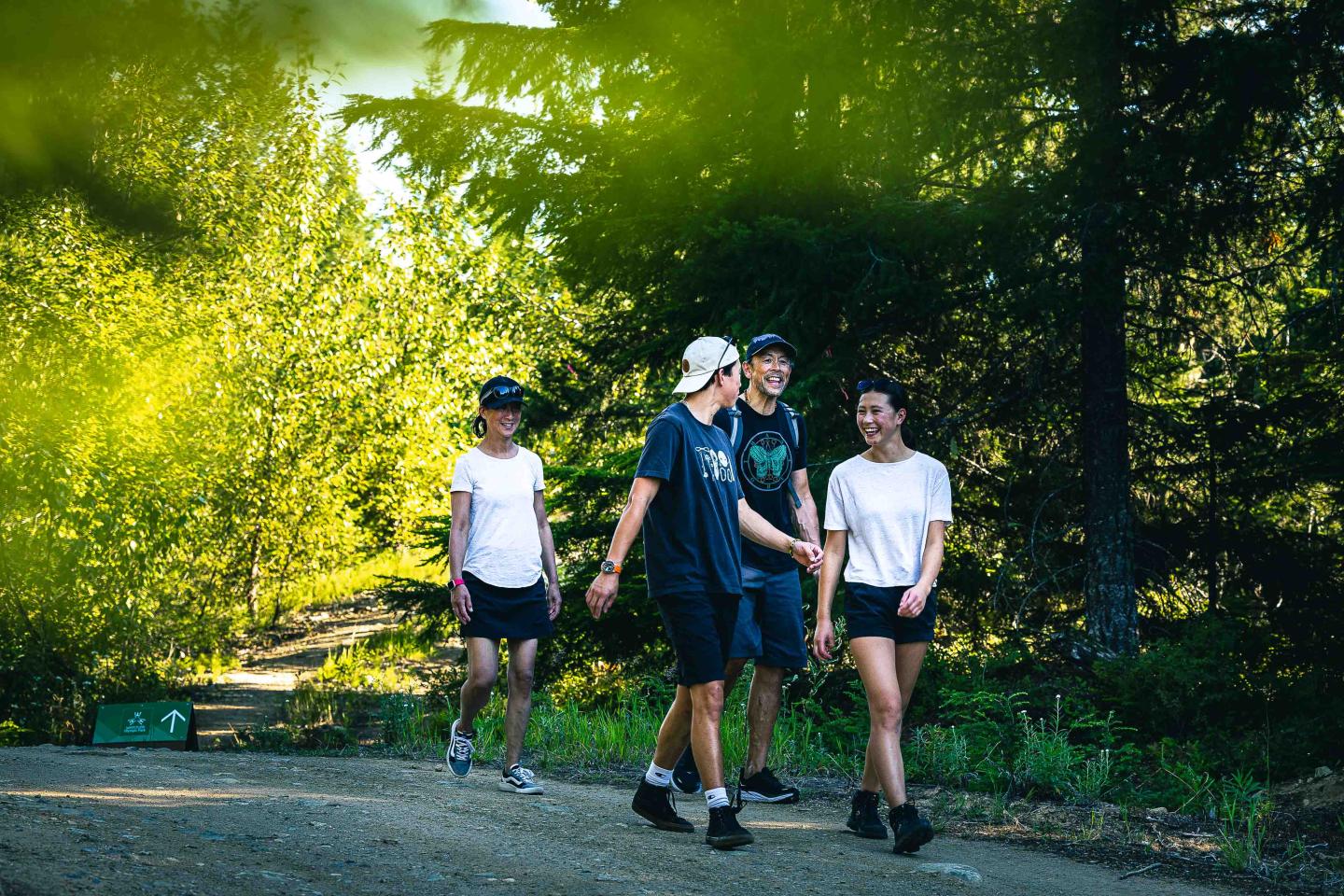 Four people walking on a forest path, wearing casual sportswear.