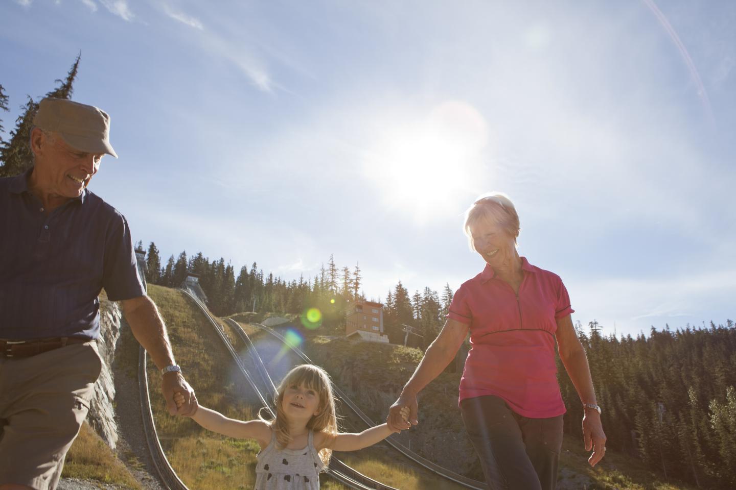 A family walks in the sunlit countryside, holding hands and smiling.