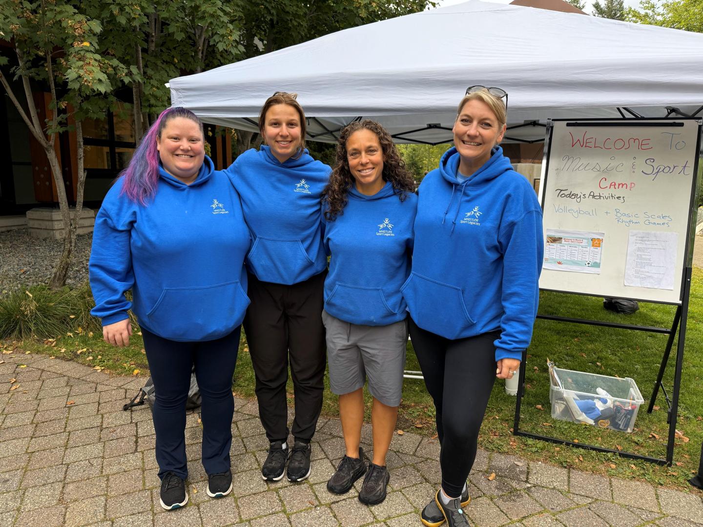 Four people in blue hoodies stand smiling under a canopy.