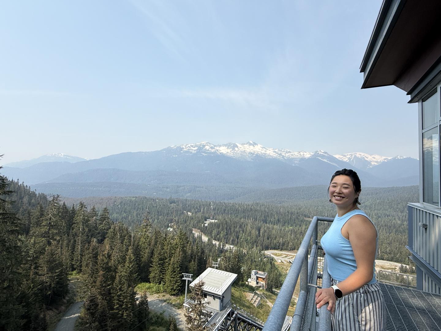 Smiling person on balcony, overlooking forest and mountains.