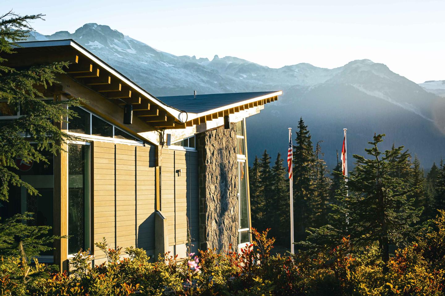 Whistler Olympic Park Day Lodge  building with mountain backdrop, surrounded by forest, flags in front.