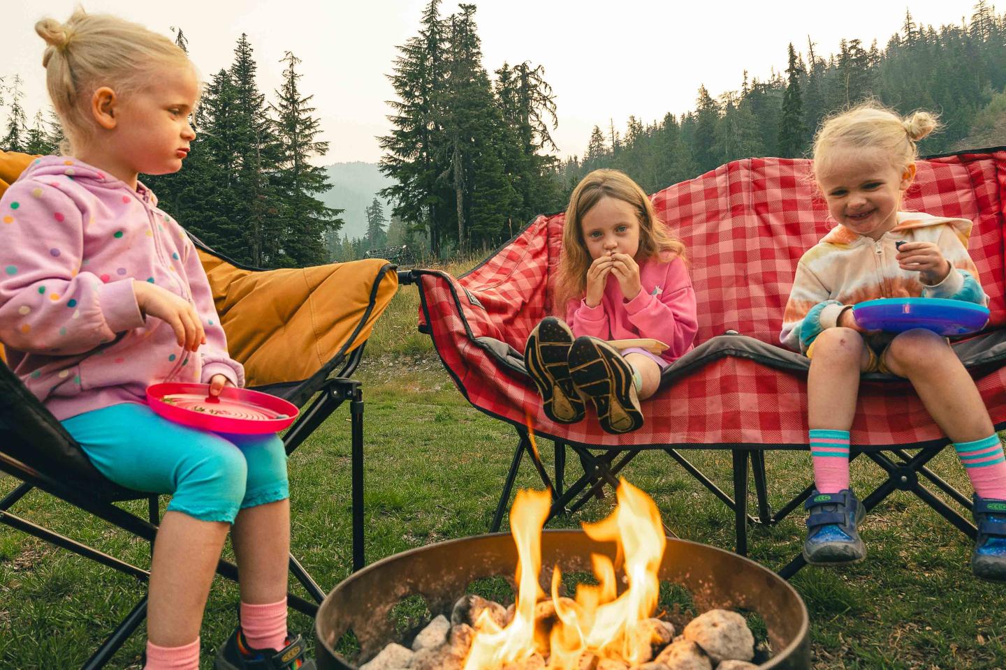 Whistler Olympic Park Three children sit around a campfire in a forest setting, holding bowls.