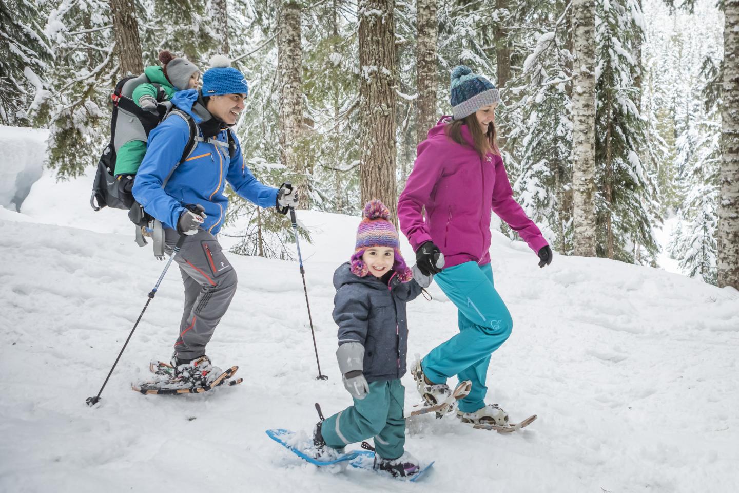 Family snowshoeing through a snowy forest.